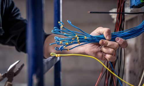 A construction electrician cuts a voltage cable during a repair, close up.