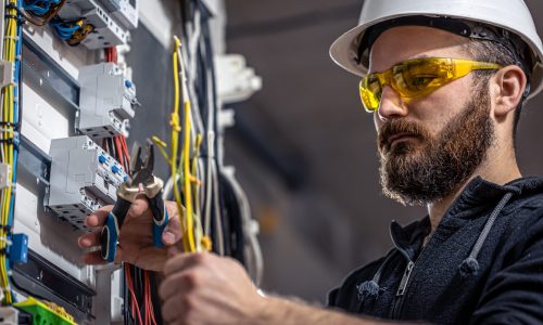 Male electrician at the checkout counter on a blurred background of a switchboard.